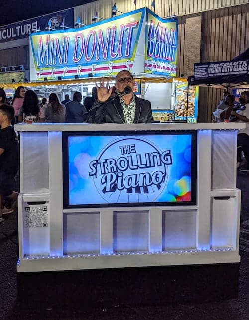Pianist sits behind white piano with neon sign