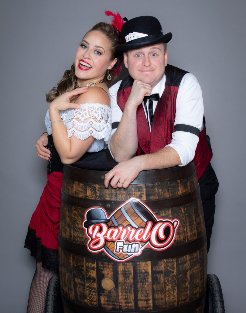 Man and woman dressed in old-fashioned western saloon wear pose near a barrel